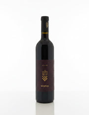A bottle of Gospoja Cuvés red wine stands on a cardboard box in a warehouse setting, with other bottles and shelving visible in the background.