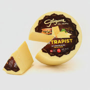 Round Gligorie Trappist cheese with a wedge on a white background