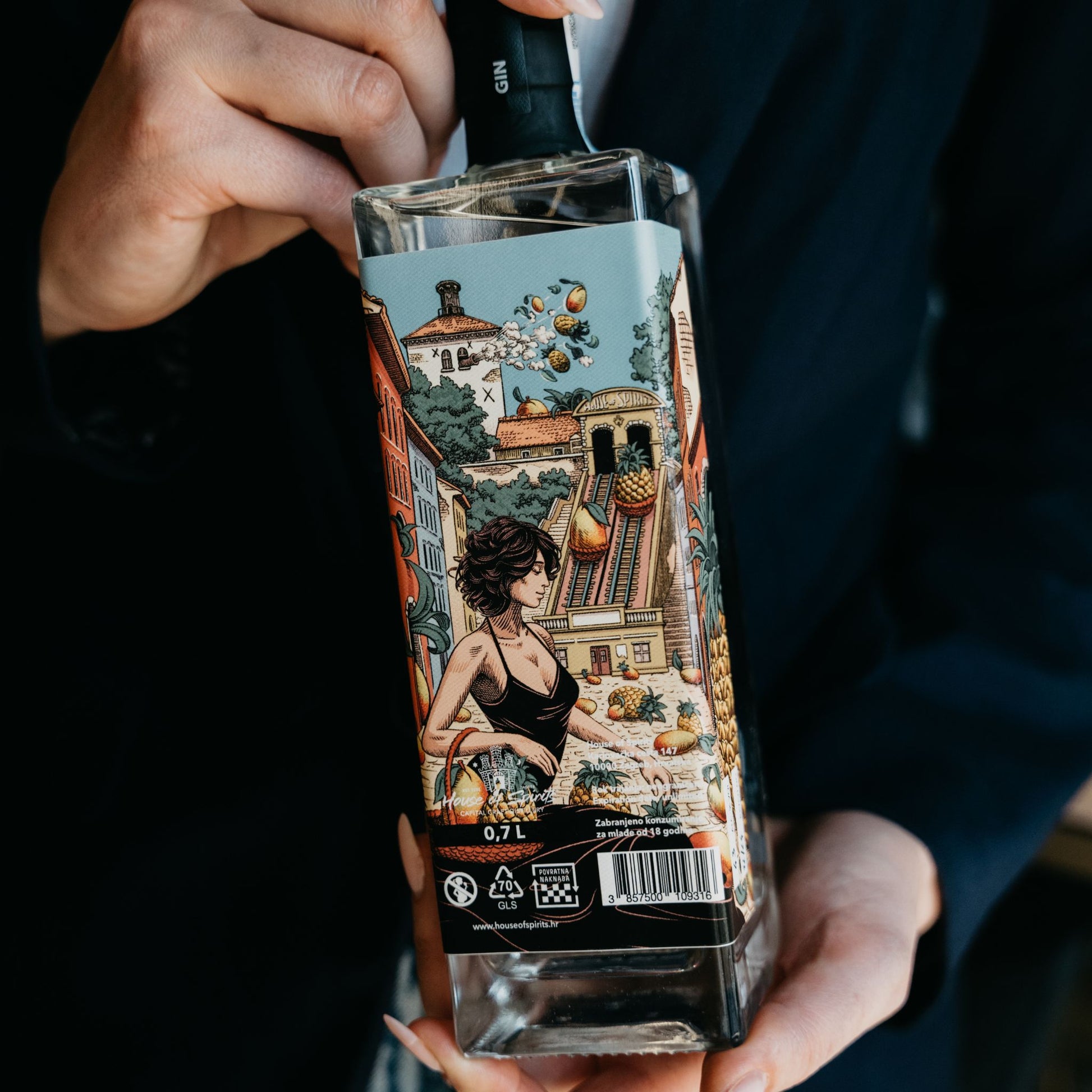 Person holding a decorative bottle with an intricate label featuring a woman and architectural elements.